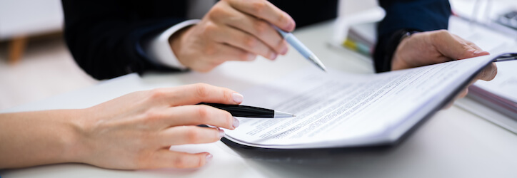 Two-Businesspeople-Hand-Analyzing-Document-Over-Glass-Desk